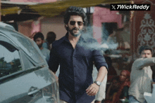 a man wearing sunglasses and a watch stands in front of a sign that says 7wick reddy