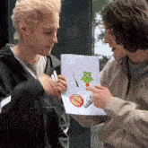 two men are looking at a drawing of a frog with a knife