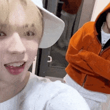 a man wearing a white hat and an orange hoodie is taking a selfie with another man .