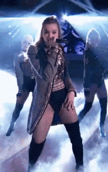 a woman is dancing on a stage with two other dancers behind her