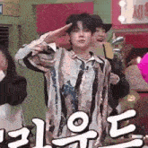 a young man in a striped shirt is saluting while standing in front of a group of people .