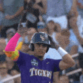 a baseball player wearing a purple tigers jersey is standing in front of a crowd .