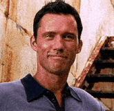 a man in a purple shirt is smiling in front of a rusty wall .