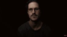 a man wearing glasses and a black shirt is making a gesture with his hands