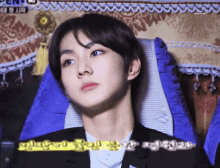 a young man in a suit sits in a chair with a blue cushion and a sign that says pen