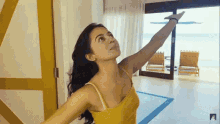 a woman in a yellow tank top is reaching up towards the sky