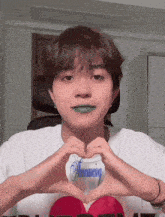 a young man with green lipstick making a heart shape