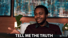 a man is sitting in front of a sign that says " tell me the truth "