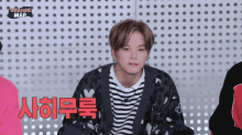 a young man wearing a striped shirt and a black cardigan is sitting in front of a wall with polka dots .