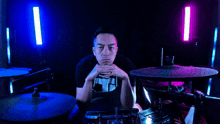 a man is sitting in front of a drum set with a purple light behind him