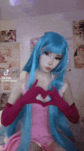 a girl with blue hair and pink gloves is making a heart with her hands .
