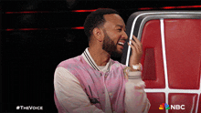 a man wearing a pink and white jacket is laughing in front of a nbc logo