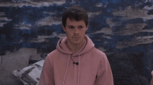 a young man wearing a pink hoodie is standing in front of a blue wall