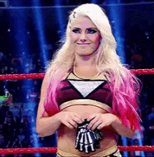 a blonde woman with pink hair is standing in a ring holding a pair of gloves