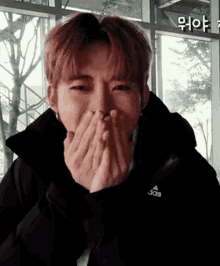 a young man is covering his mouth with his hands and laughing .