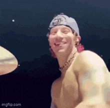 a shirtless man is playing drums and smiling while wearing a hat .