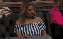 a woman is sitting on a couch wearing a striped off the shoulder top