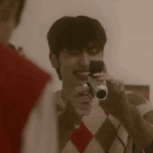 a man is taking a picture with a camera while wearing a plaid sweater .