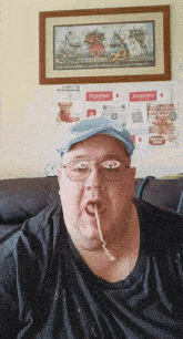 a man wearing glasses and a blue hat is eating noodles in front of a framed picture of a teddy bear