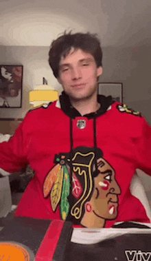 a man wearing a red chicago blackhawks sweatshirt is standing in a living room .