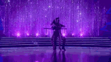 a man and woman are dancing on a stage in front of a purple background .