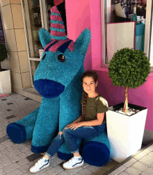 a girl sits next to a blue stuffed unicorn statue