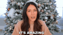 a woman is standing in front of a christmas tree and says it 's amazing