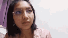 a woman wearing glasses and a pink shirt is sitting on a bed .