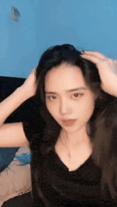 a woman in a black shirt holds her hair in her hands