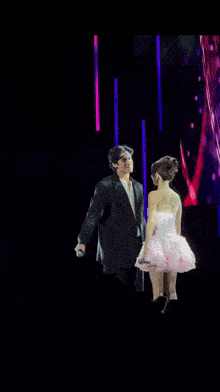 a man in a suit is standing next to a woman in a pink dress on a stage .