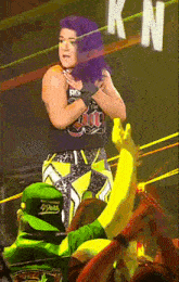 a woman in a wrestling ring is being lifted by a man in a green hat with the letter k on it
