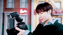 a young man is holding a camera in front of a building with a red sign that says ' lotto ' on it .