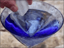 a person is pouring ice into a martini glass that is filled with blue liquid