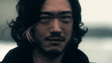 a man with long black hair and a beard looks at the camera