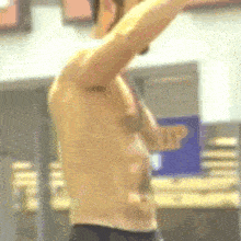 a man without a shirt is standing in a gym with his arms outstretched .