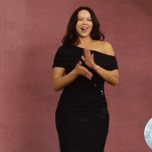 a woman in a black dress is clapping her hands in front of a red background