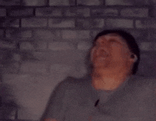 a man wearing earbuds is sitting in front of a brick wall and looking at the camera .