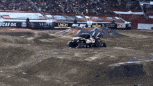 a monster truck is driving down a dirt track in front of a banner that says lucas oil