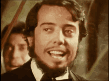 a man with a beard is smiling with a man in the background