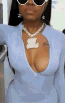 a woman wearing a blue dress and sunglasses is taking a selfie with her breast exposed .