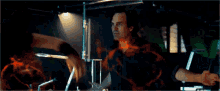 a man in a black shirt is surrounded by flames in a dark room