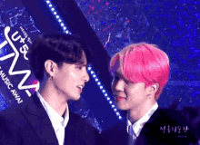 two men with pink hair are standing next to each other in front of a sign that says music away