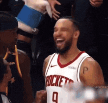 a man wearing a rockets jersey is laughing with his fist in the air