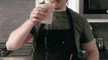 a man in an apron is drinking a milkshake from a glass with a straw .