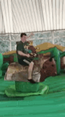 a man in a green shirt is riding a bull on a green mat .