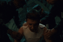 a man in a white tank top is being helped by two men .