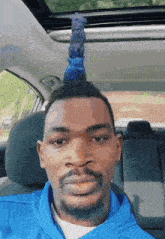 a man in a blue hoodie is sitting in the driver 's seat of a car with his hair in a mohawk .
