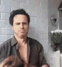 a man without a shirt is sitting in front of a brick wall .