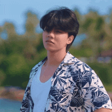 a man wearing a blue and white floral shirt stands in front of a body of water