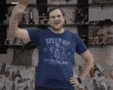 a man wearing a blue speed up shirt is waving his hand